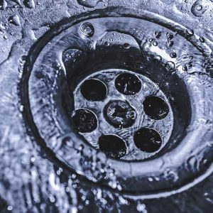 Close-up of a sink drain with running water, illustrating home drain maintenance and cleaning tips.