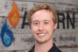 Acorn Heating and Plumbing technician Nolan in front of company logo wall background.