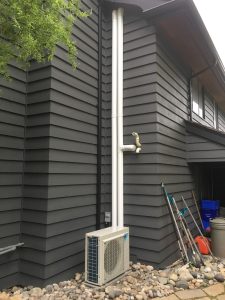 Daikin heat pump installed on exterior wall of a modern grey home by Acorn Heating and Cooling.