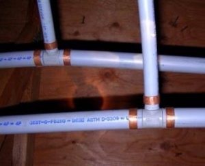 Poly-B plumbing pipes with copper fittings installed along a wooden joist, showing an older piping system common in BC homes.